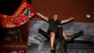 Ein Liverpool-Fan feiert den Gewinn der Premier League, als er auf einer Statue von Bill Shankly außerhalb von Anfield sitzt