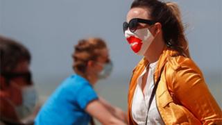 Ein Tourist mit einer schützenden Gesichtsmaske geht in Belgien am Strand entlang, als er in die Quarantäneliste Großbritanniens aufgenommen wurde